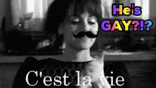 a woman with a fake mustache is holding a cat with the words he 's gay behind her
