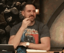 a man wearing a star wars t-shirt is sitting at a table with his hand on his chin .