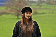 a woman wearing a black hat and a black coat is standing in a field