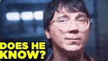a man wearing glasses is looking at the camera with the words `` does he know '' written above him .