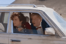 two men are sitting in a car and one of them is wearing a bow tie .