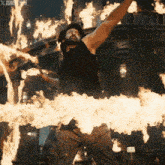 a man in a black tank top is surrounded by flames with xtoms 2015 written on the bottom right