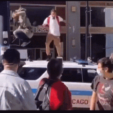 a man is standing on the roof of a police car talking on a cell phone .