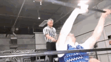 a referee is standing next to a wrestler in a ring holding a sword .