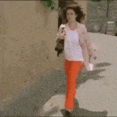 a woman in a pink coat and orange pants walking down a street