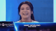 a woman is laughing while sitting in front of a sign that says marc noveloso head writer .