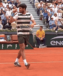 a man in a striped shirt is walking on a tennis court in front of an enc banner