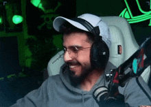 a man with a beard is wearing headphones and a hat while sitting in front of a microphone .
