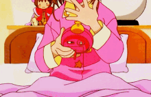 a girl in a pink pajamas is sitting on a bed holding a pink clock