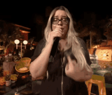 a woman wearing glasses is singing into a microphone at night
