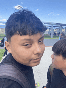 a boy with a backpack looks at another boy while standing on a sidewalk
