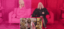two drag queens are sitting on a couch in a pink room .
