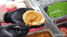 a person wearing black gloves is holding a piece of bread with sauce on it