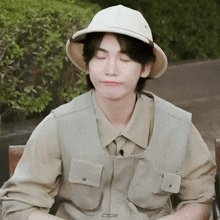 a man wearing a hat and a vest is sitting on a chair