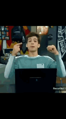 a young man sitting in front of a laptop with his arms outstretched