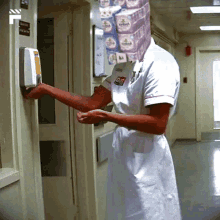 a nurse is washing her hands in a hallway with a stack of wipes on the wall