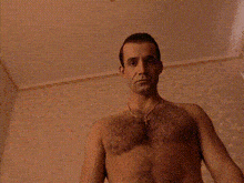 a shirtless man with a necklace around his neck is taking a selfie