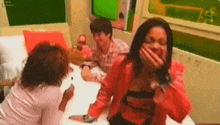 a woman in a red jacket is covering her mouth with her hand while sitting on a bed .