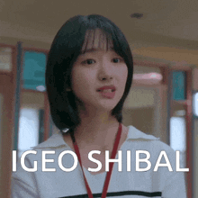 a woman with short hair is wearing a red lanyard and making a funny face while standing in a hallway .