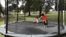 two children are playing on a round trampoline in a park