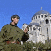 a man in a green jacket is standing in front of a large building .