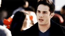 a young man in a black jacket and blue shirt is talking to another man .