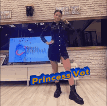 a woman in a black dress stands in front of a tv screen that says " princess vot " on it