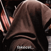 a person with a hood on their head and the words fakecel written on their face .