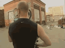 a man in a black nike tank top stands in front of a building with graffiti on it