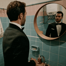 a man in a tuxedo is looking at himself in a bathroom mirror