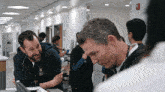 a man with a stethoscope around his neck talks to another man in a hospital hallway