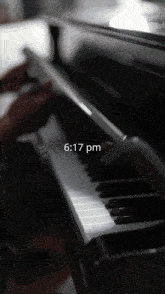 a person is playing a piano with the time of 6:17 pm