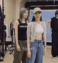 two women are standing next to each other in a room and one of them is wearing a baseball cap .