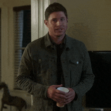 a man in a green jacket holds a cup in his hands