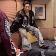 a man in a leather jacket is sitting on a couch with other people .
