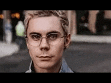 a young man wearing glasses is standing on a street .