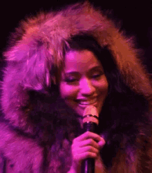 a woman in a fur coat is singing into a microphone while wearing a fur hood .