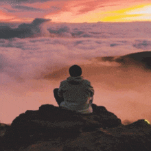 a man is sitting on top of a mountain looking at the clouds at sunset