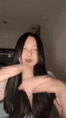 a young woman with long black hair is making a funny face while making a peace sign with her hands .