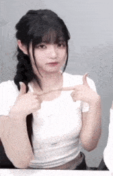 the girl is wearing a white shirt and braided hair and is pointing at herself .