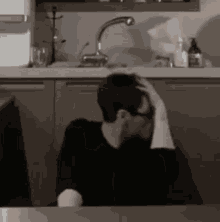 a man is sitting at a table in a kitchen and holding his head .