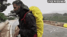 a man with a yellow backpack is walking down a road with the words viperissima written above him