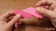 a person is holding a piece of pink paper in their hands and the words made in animotica are on the bottom