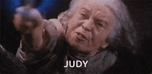 an elderly woman is pointing at the camera with the word judy written below her .