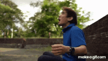 a man in a blue shirt is sitting on the ground with his mouth open and a watch on his wrist