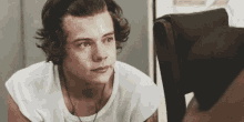 harry styles is wearing a white t-shirt and looking at the camera .