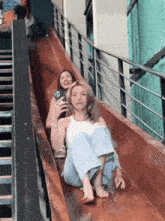 two women are sitting on a wooden slide and one is taking a picture of herself