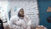 a man in a hoodie is sitting in front of a brick wall .