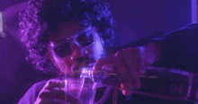 a man with curly hair is drinking from a bottle while wearing sunglasses and a purple wig .