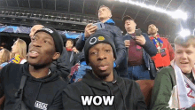 a group of people are sitting in a stadium and one of them is wearing a hat that says wow on it